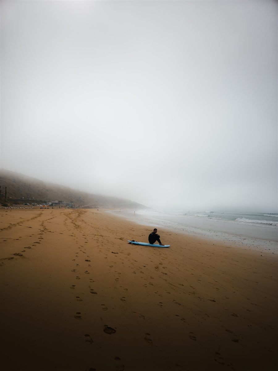 Surfer sitting on his board on a misty beach