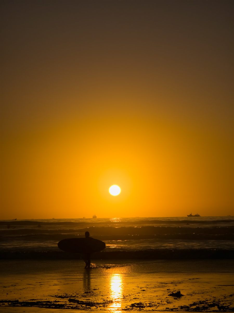 Surfer walking out of the sea at sunset